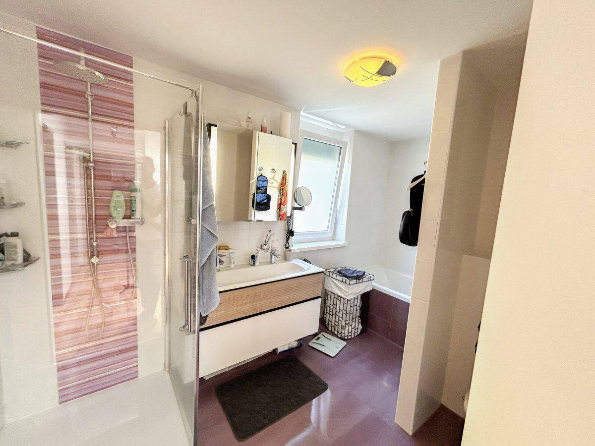 Modernes Badezimmer mit Dusche, Badewanne, Waschtisch und Fenster für Tageslicht.