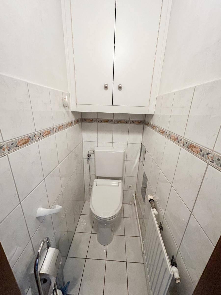 Separates WC mit wandhängender Toilette, Fliesen und einem praktischen Spiegelschrank.