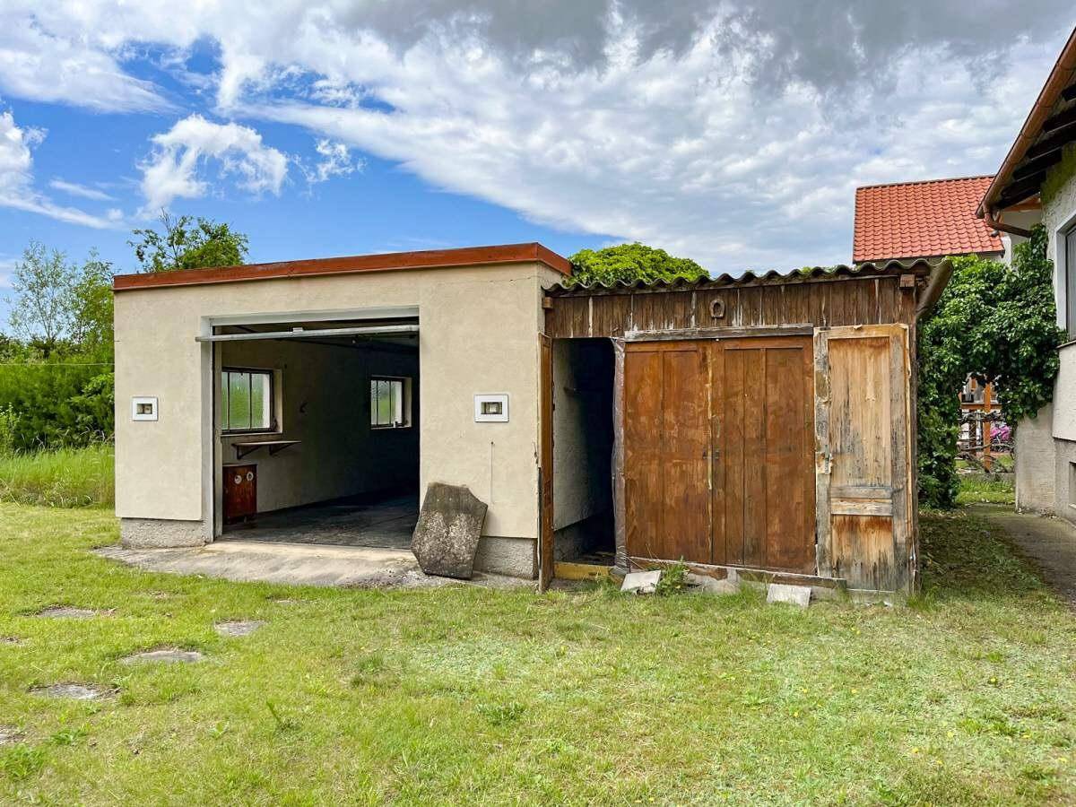 Freistehende Garage und ein Holzschuppen auf einer grünen Rasenfläche.