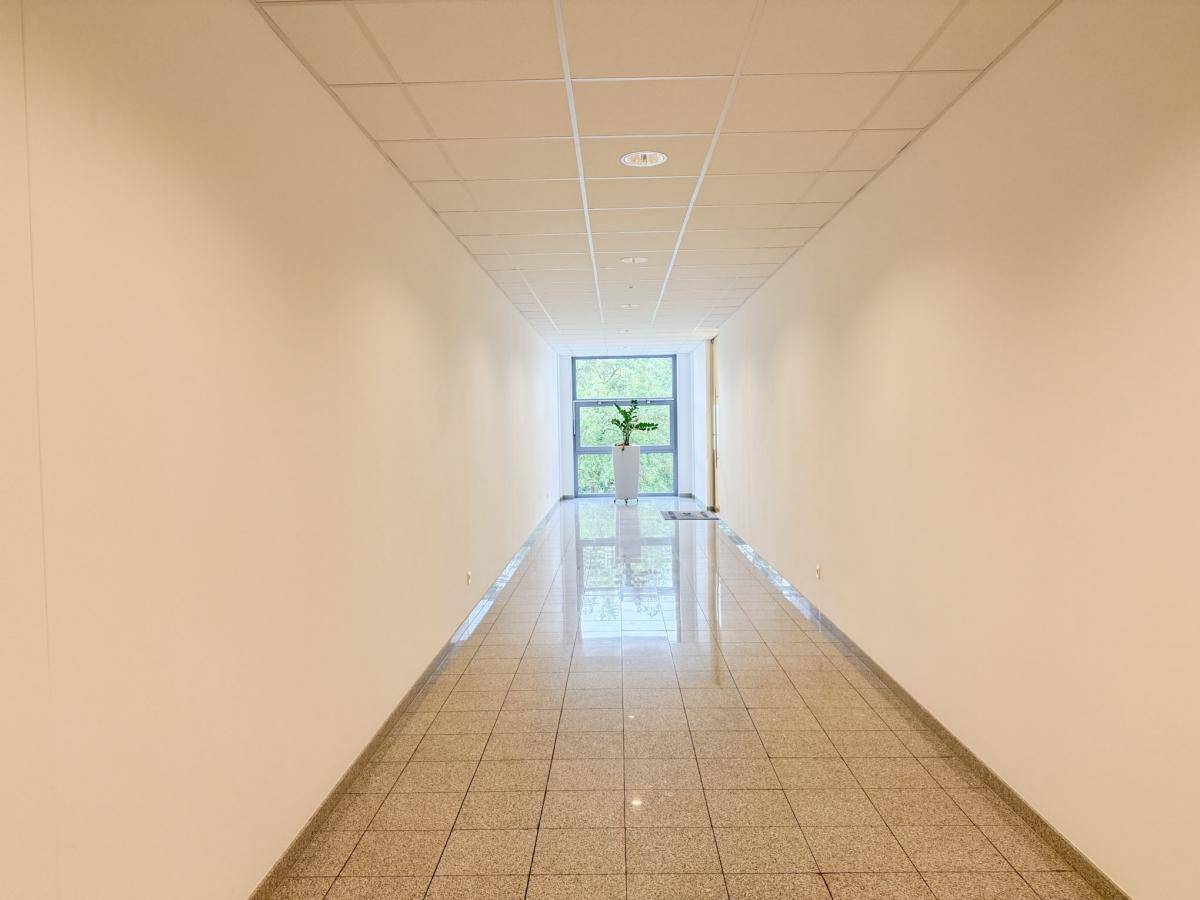 Langer, heller Flur mit Fliesenboden und einem Fenster am Ende, das ins Grüne blickt.