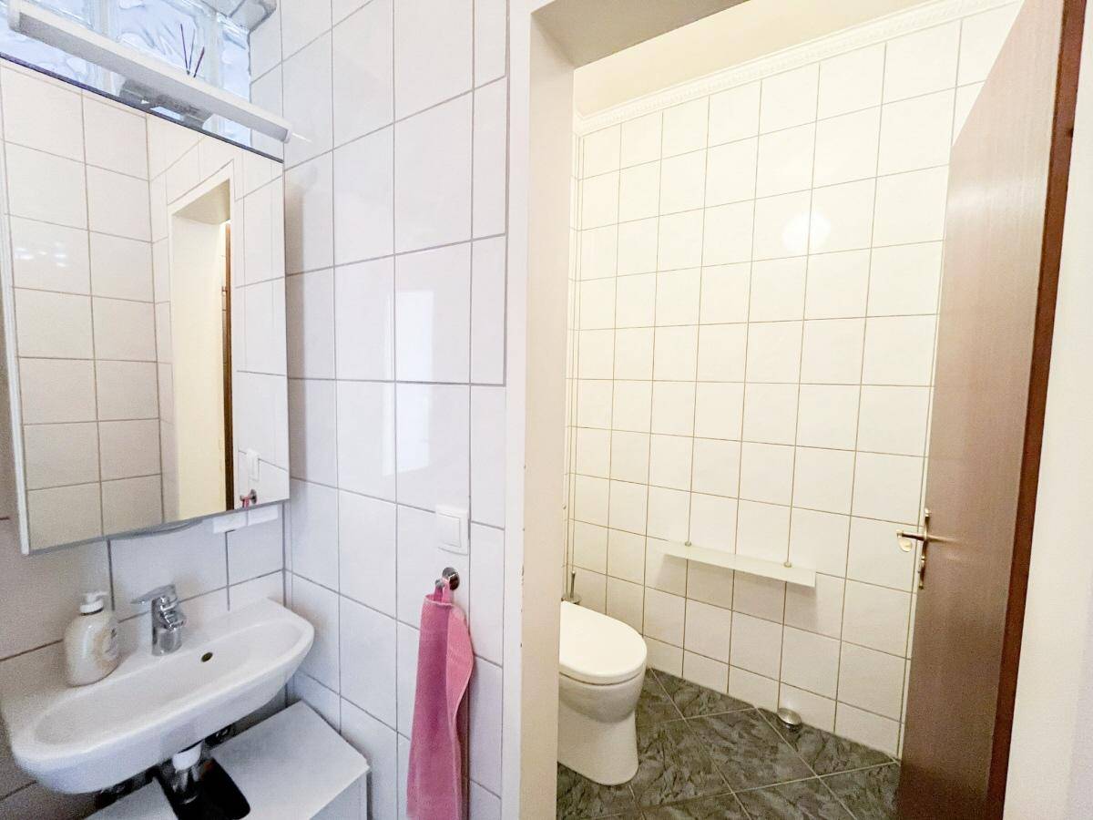 Kleines Gäste-WC mit weißen Fliesen, Waschbecken und Toilette.