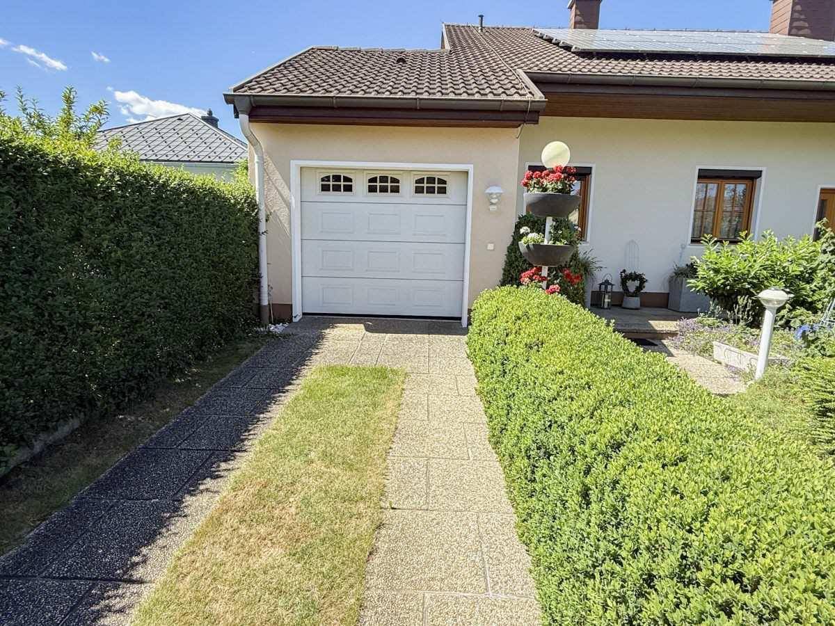Einfahrt zur Garage mit gepflegter Hecke und Blumenarrangements.