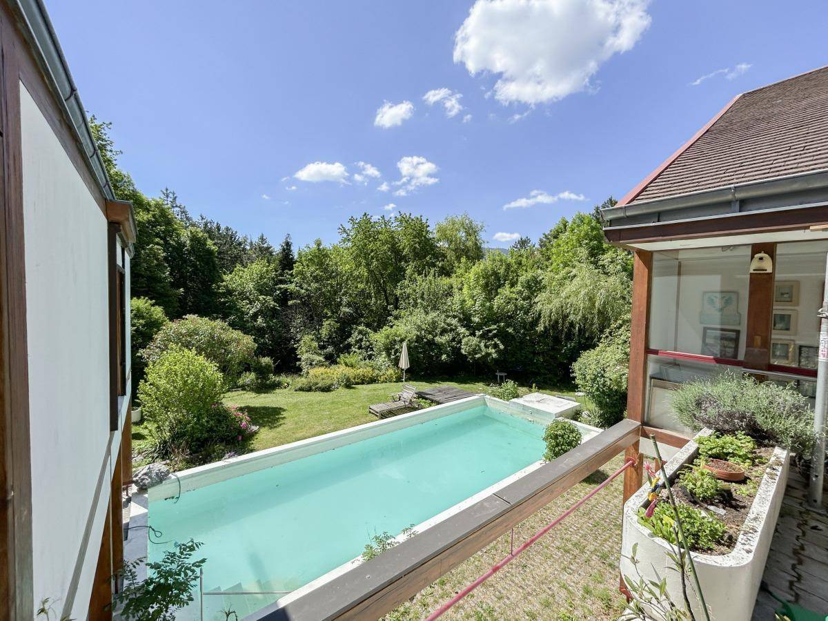 Blick von der Terrasse auf den Pool und den weitläufigen Garten mit üppiger Vegetation.