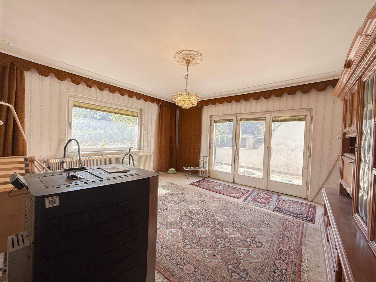 Geräumiges Wohnzimmer mit Kaminofen, Teppichboden und Zugang zur Terrasse.