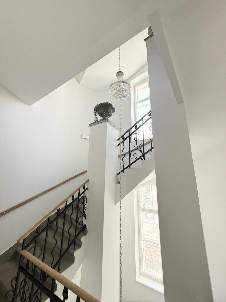 Elegantes Treppenhaus mit schmiedeeisernem Geländer, hohen Decken und einem Kronleuchter.