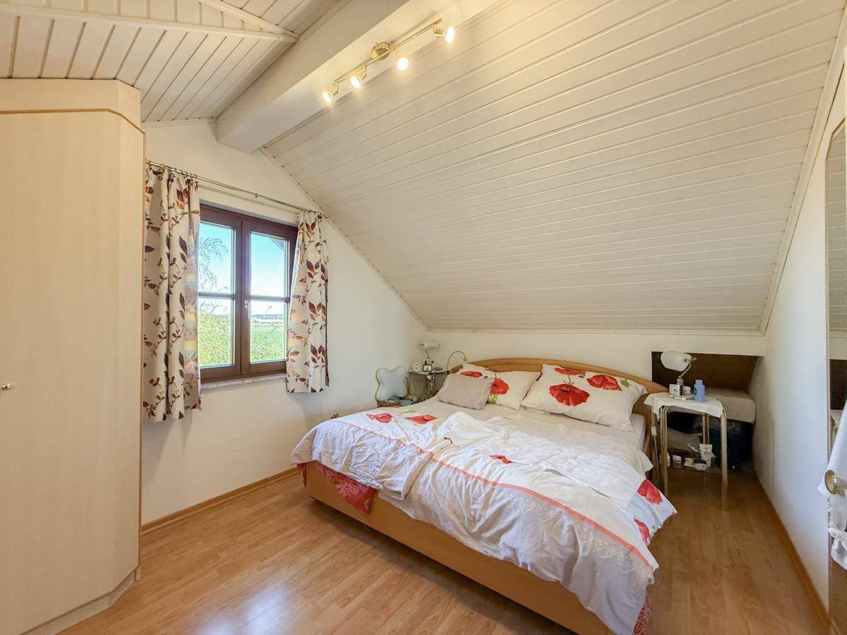 Gemütliches Schlafzimmer im Dachgeschoss mit schräger Decke, Holzpaneelen und Doppelbett.