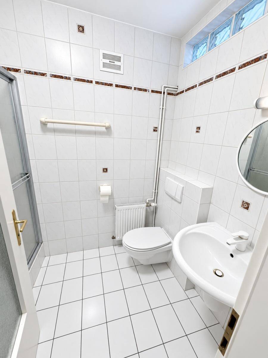 Gefliestes Badezimmer mit Dusche, WC, Waschbecken und einem kleinen Fenster für Belüftung.