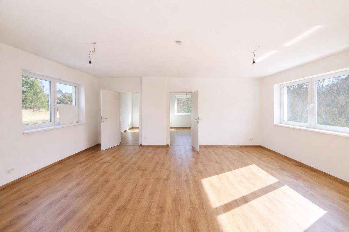 Helles, leeres Zimmer mit Laminatboden und großen Fenstern, bereit für die Einrichtung.