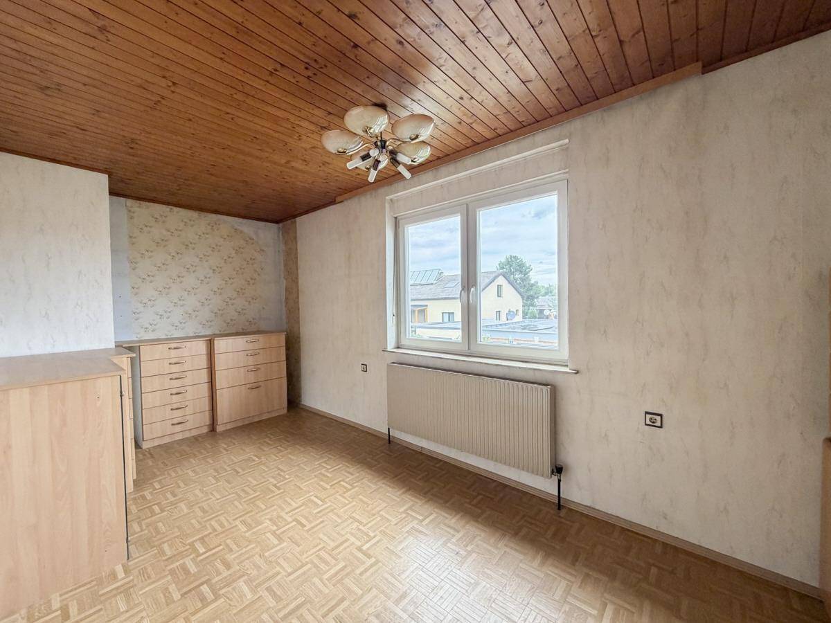 Schlafzimmer mit Holzdecke, Laminatboden und Fenster mit Blick auf die Umgebung.