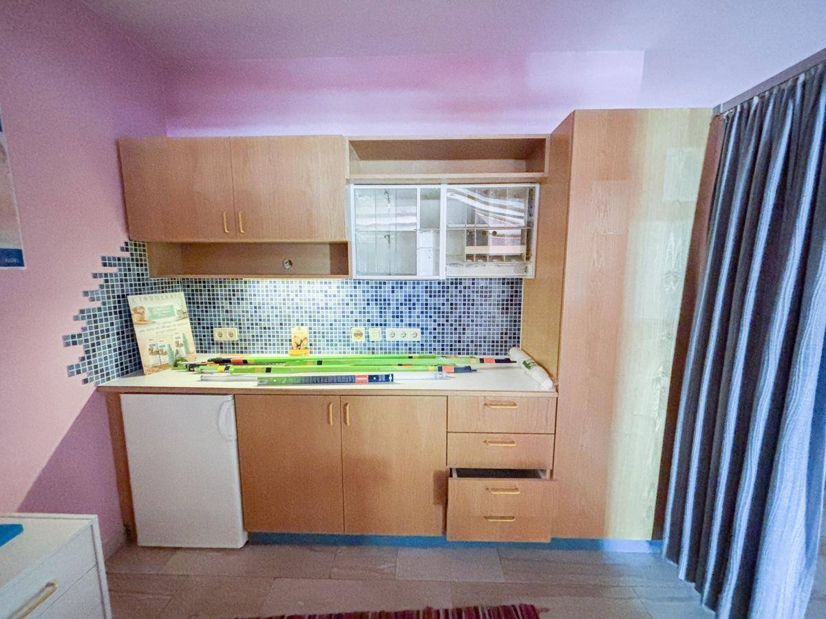 Detailansicht einer kleinen Küchenzeile mit Holzschränken, Fliesenrückwand und integriertem Kühlschrank.