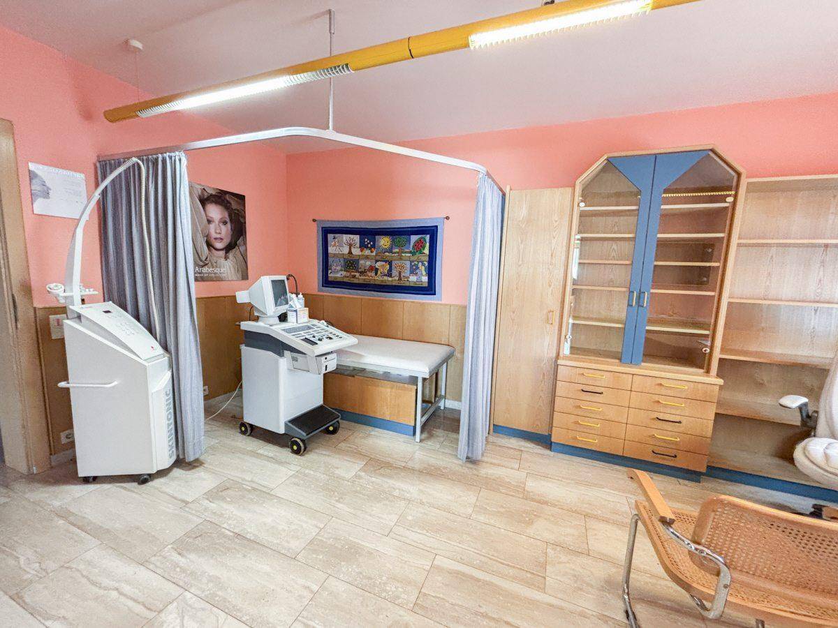 Behandlungszimmer mit medizinischen Geräten, einem Untersuchungstisch und Vorhängen für Privatsphäre.