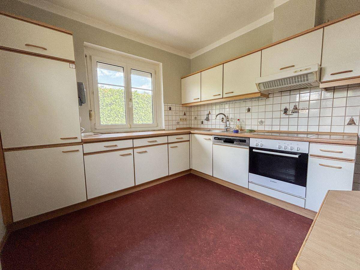 Funktionale Küche mit weißen Einbauschränken, Holz-Arbeitsplatten und Fenster.