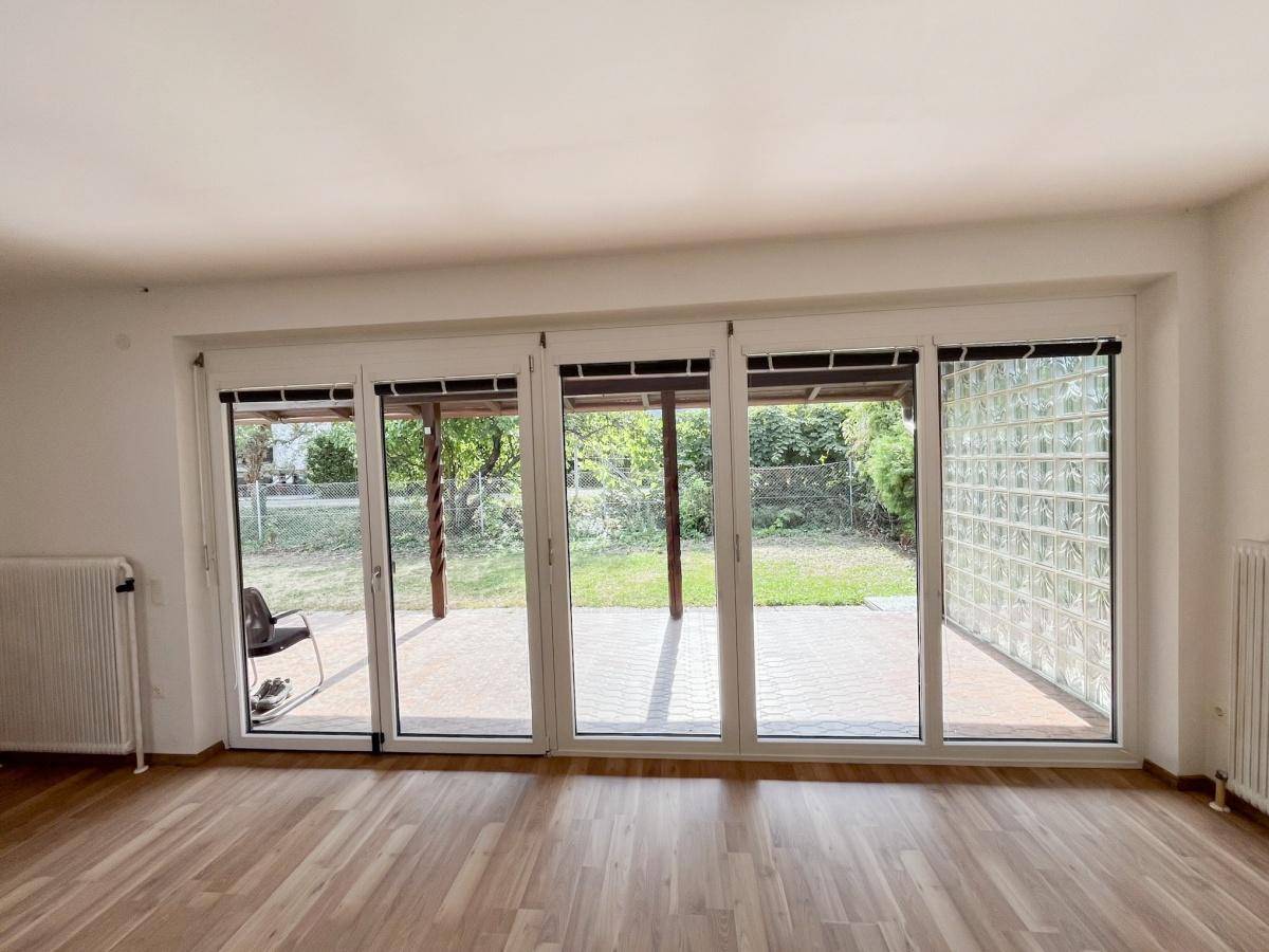 Heller Wohnbereich mit großen Fenstern, die viel Tageslicht hereinlassen und Blick in den Garten bieten.
