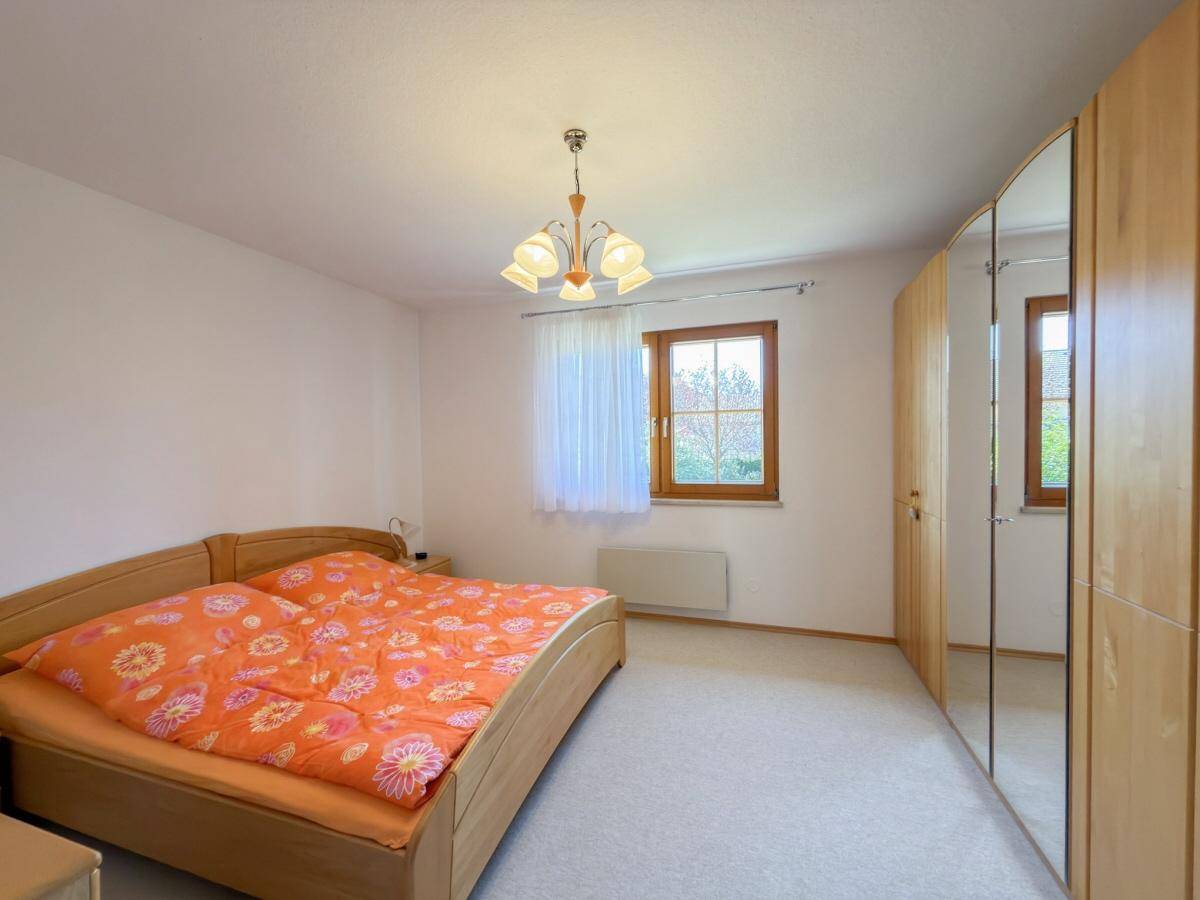 Schlafzimmer mit Teppichboden, Holzschrank und Fenster mit Blick ins Grüne.