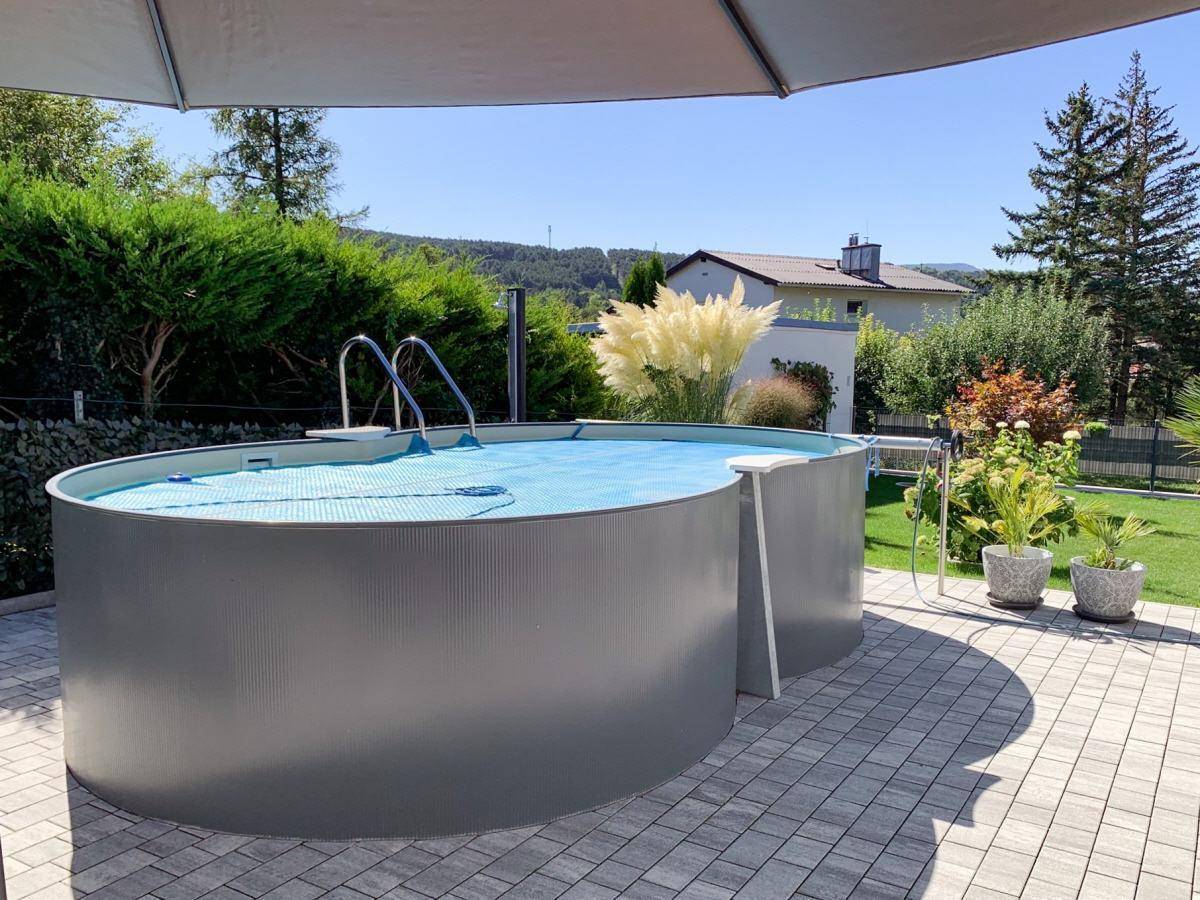 Aufstellpool auf einer gepflasterten Terrasse, umgeben von Grün und mit Blick auf die Landschaft.