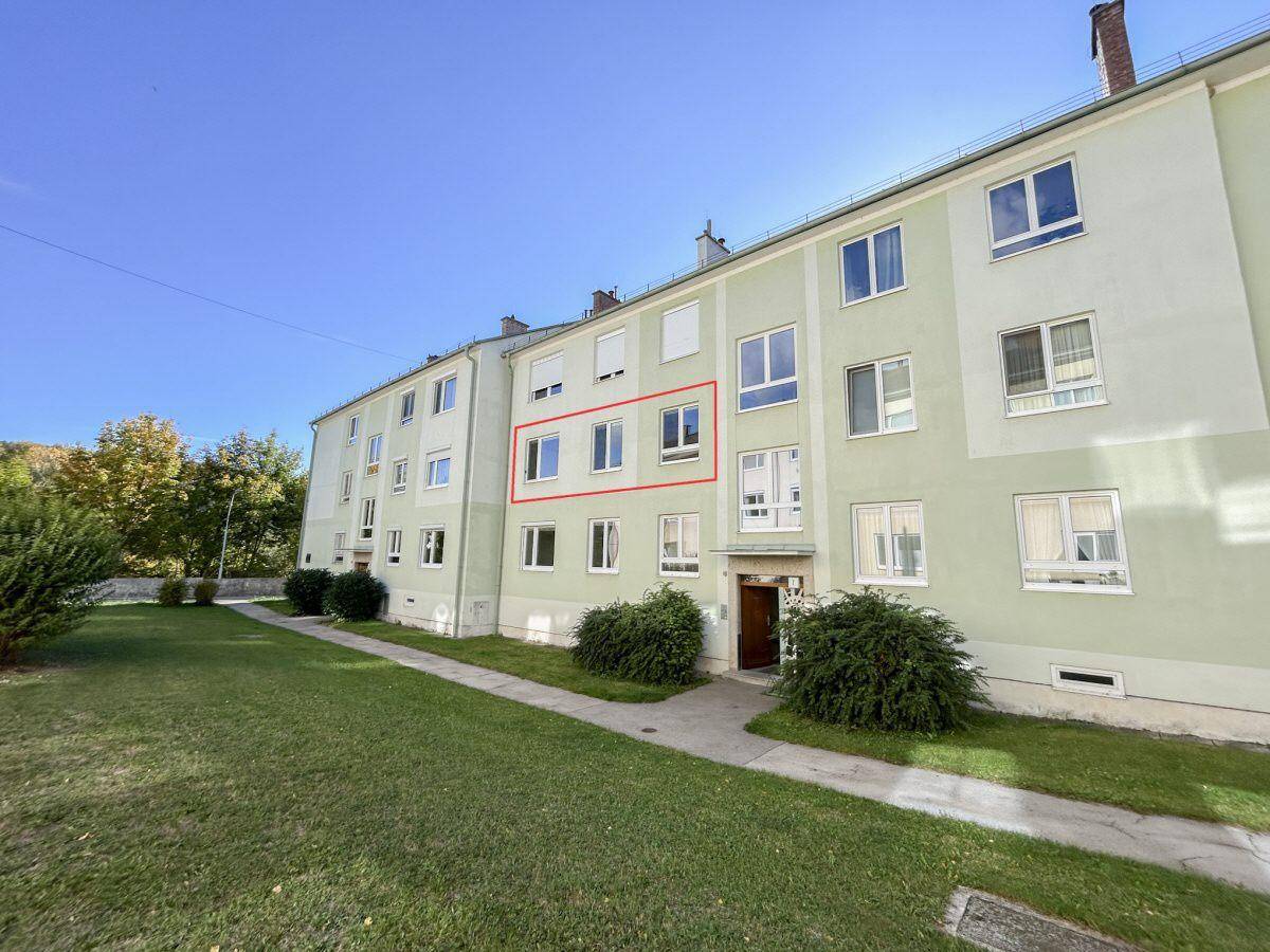 Fassade eines Wohngebäudes mit mehreren Fenstern und einer gepflegten grünen Rasenfläche davor.
