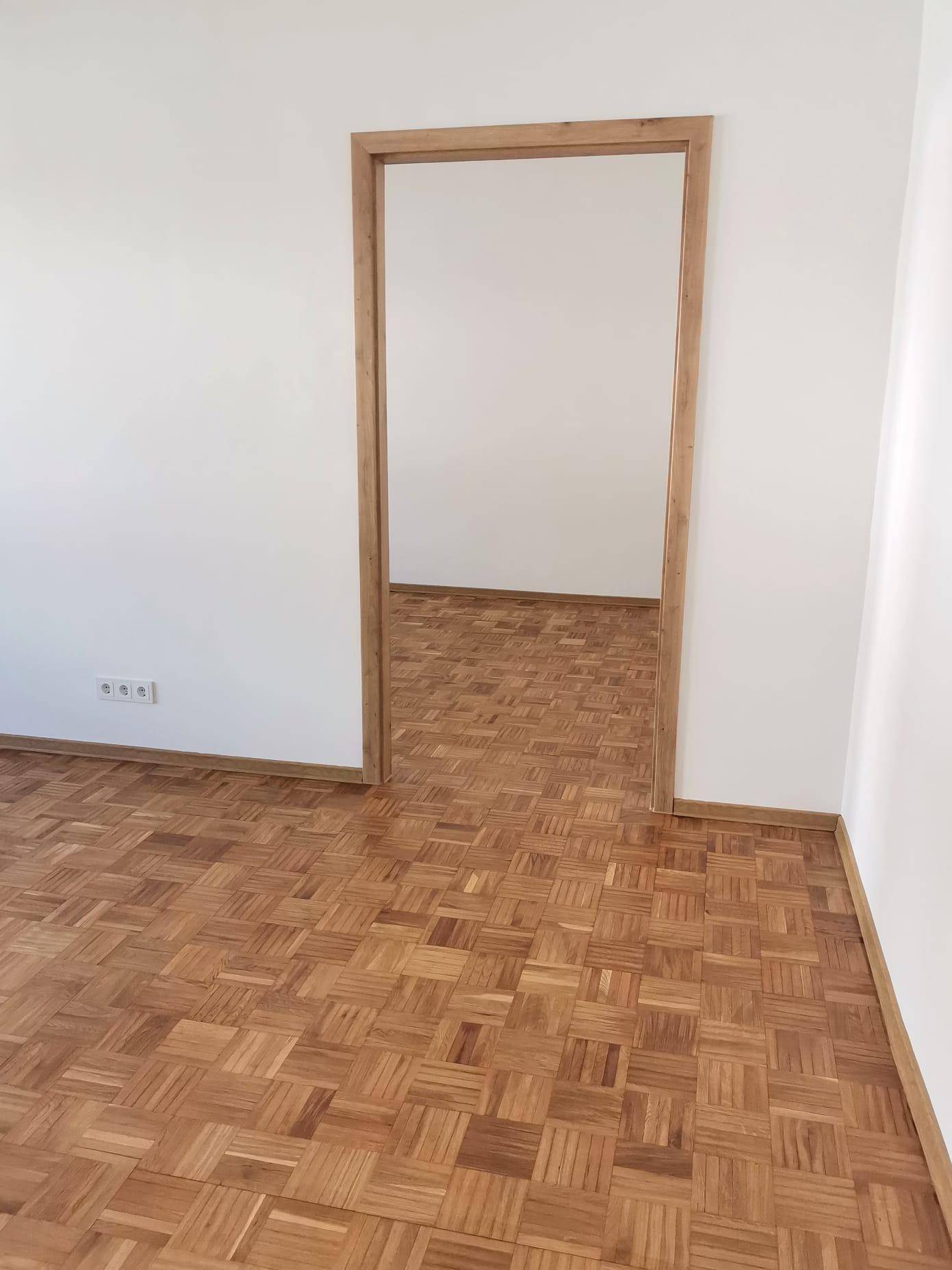 Flur mit hellem Parkettboden und Holztürrahmen, der zu einem weiteren Raum führt.