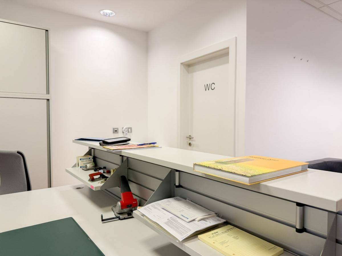 Empfangstheke in einem Büro mit Dokumenten und einer Tür zum WC-Bereich.
