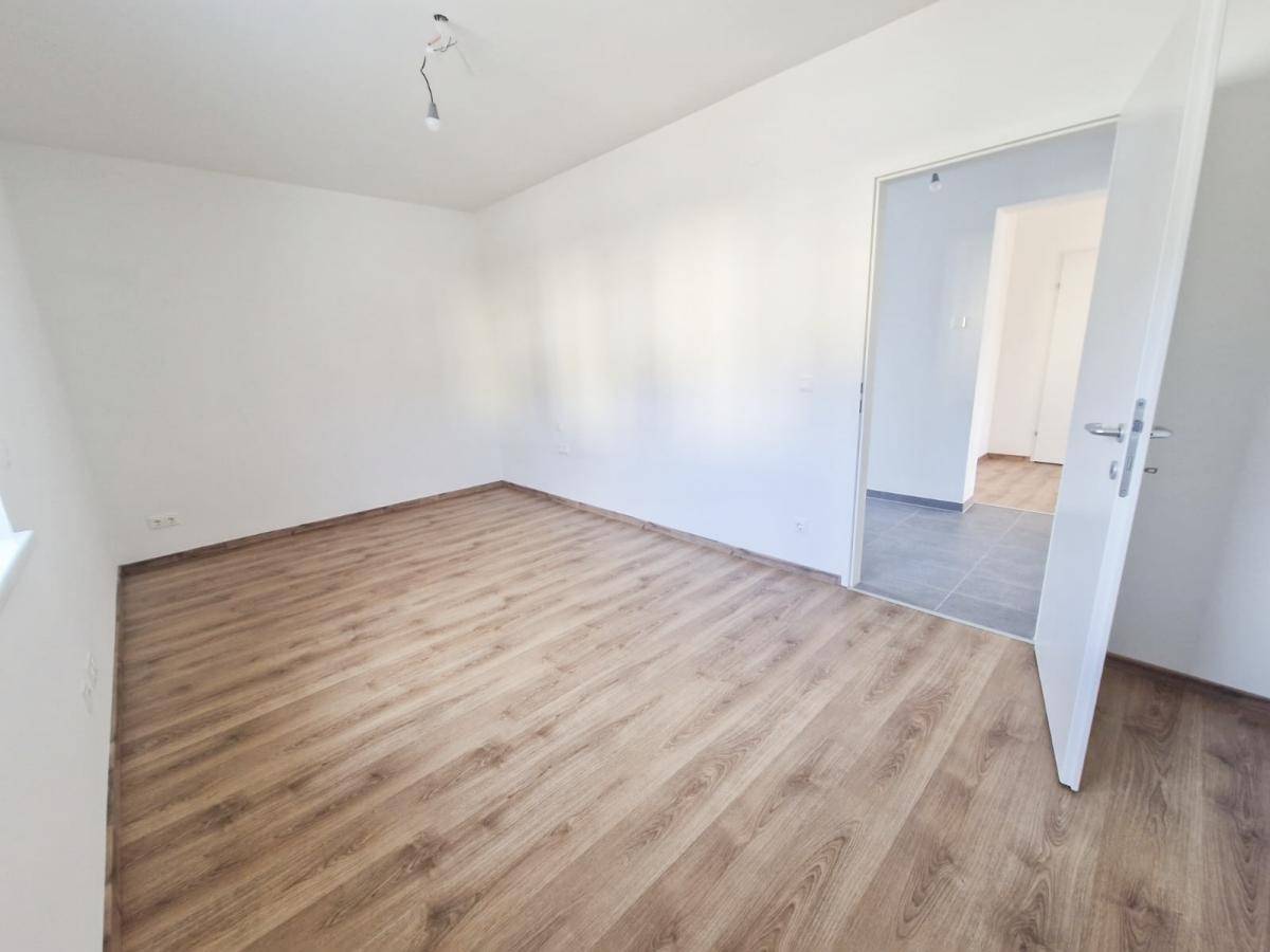 Leeres Zimmer mit Laminatboden und weiß gestrichenen Wänden, ideal als Schlaf- oder Arbeitszimmer.