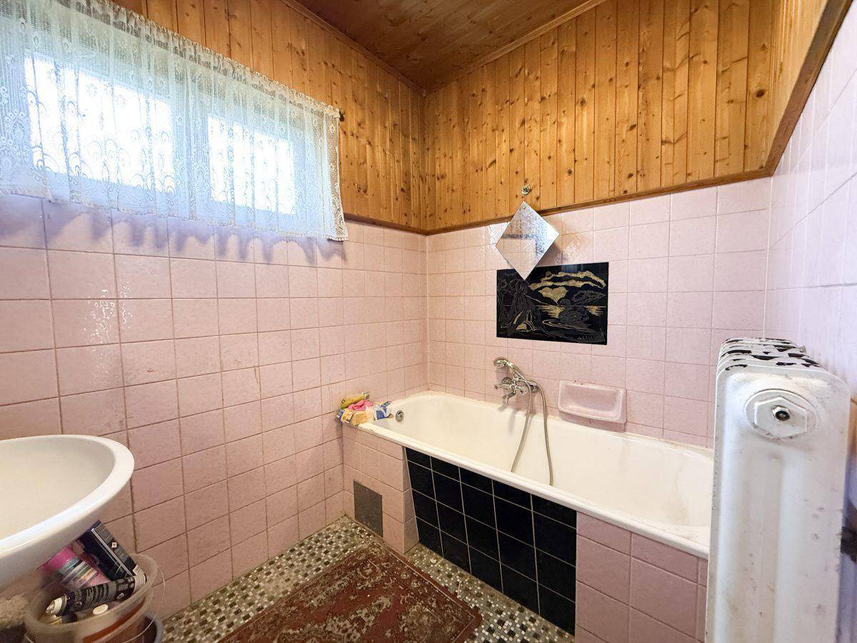 Badezimmer mit rosa Fliesen, Badewanne und Holzdecke im 80er-Jahre-Stil.