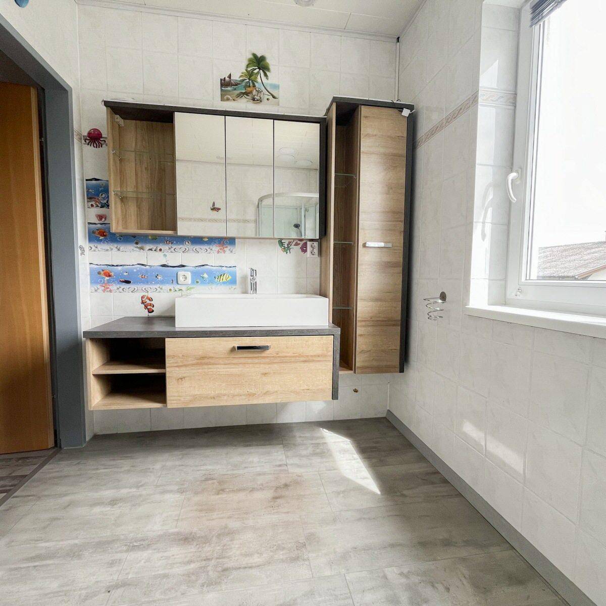 Badezimmer mit modernem Waschbecken, Spiegelschrank und Fenster, hell gefliest.