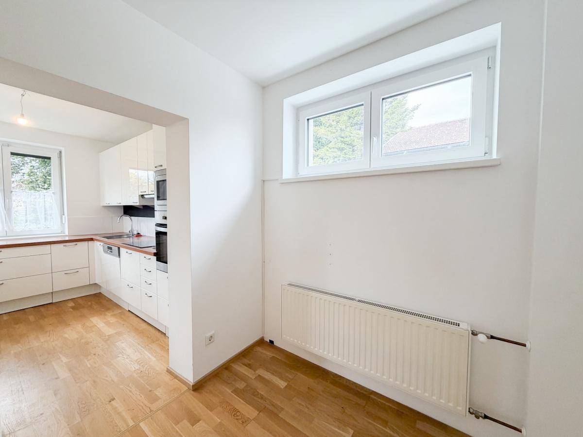 Heller Küchenbereich mit Holzboden und großem Fenster, offen zum Essbereich.