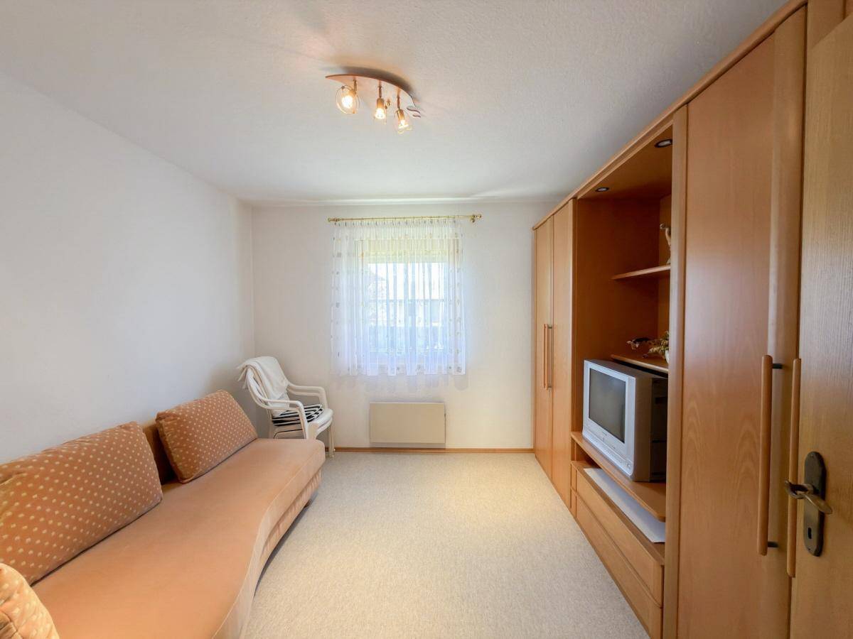 Helles Zimmer mit Teppichboden, Schrankwand und Fenster.