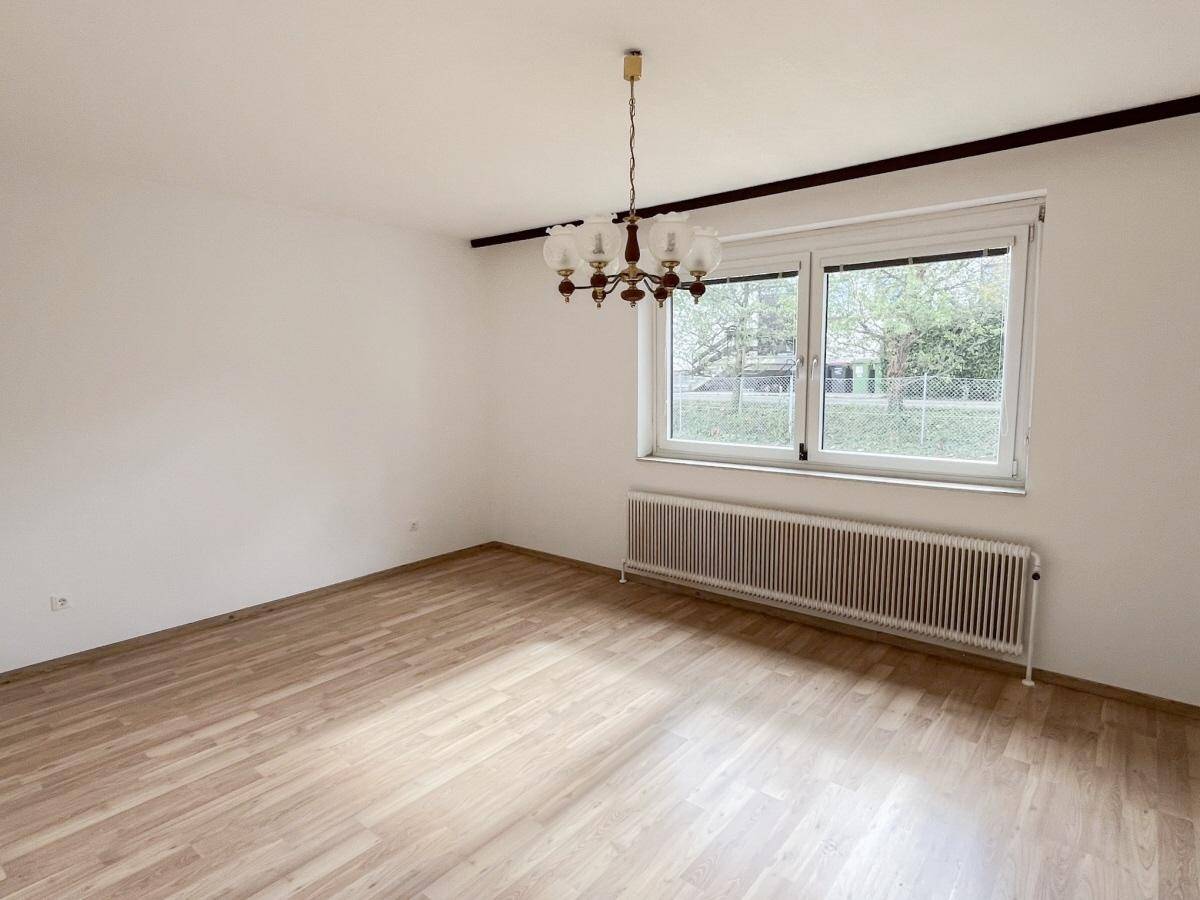 Helles Schlafzimmer mit Laminatboden und großem Fenster, das eine grüne Aussicht bietet.