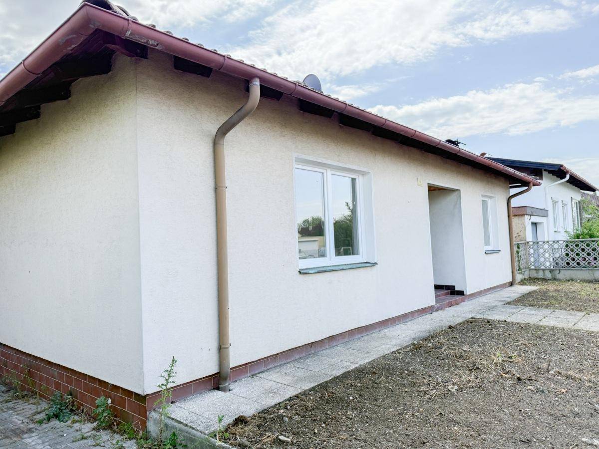 Seitenansicht des Hauses mit heller Fassade, Satteldach und gepflastertem Weg.
