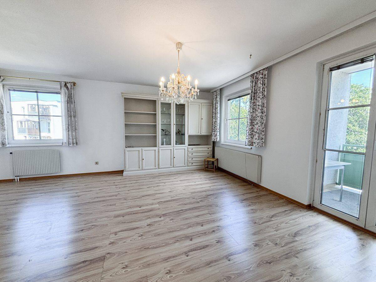 Wohnzimmer mit Laminatboden, Einbauschrank und Zugang zu einem kleinen Balkon.