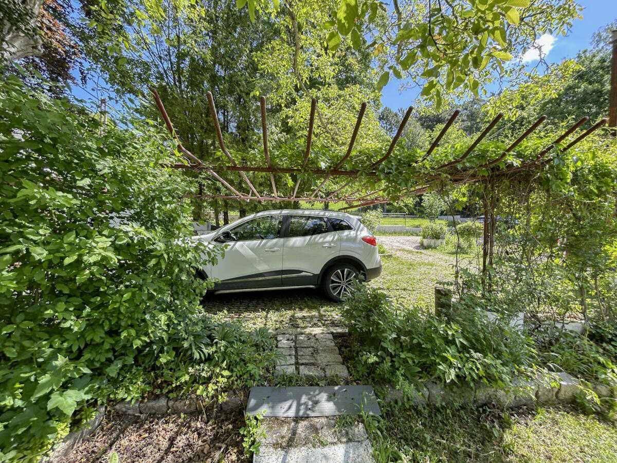 Ein Auto parkt unter einer begrünten Pergola, umgeben von üppigem Grün.