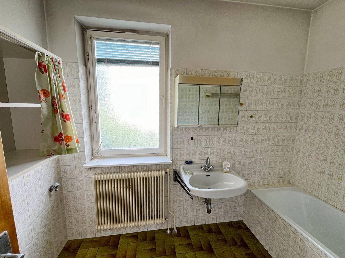Badezimmer im Stil der 80er Jahre mit Badewanne, Waschbecken und gemusterten Fliesen.