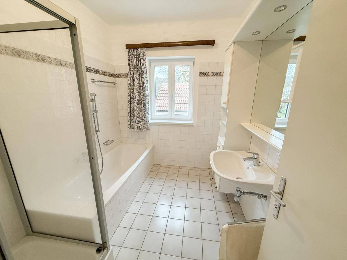 Gefliestes Badezimmer mit Badewanne, Duschkabine, Waschbecken und Fenster für Tageslicht.