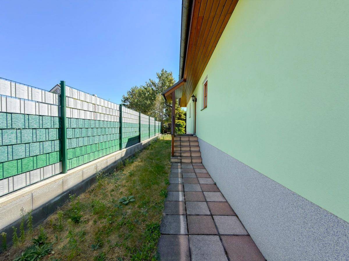 Seitenansicht des Hauses mit gepflastertem Weg und grünem Zaun.