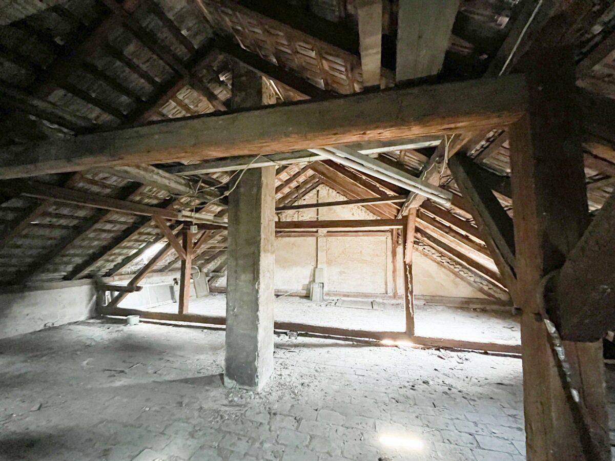 Geräumiger Dachboden mit sichtbaren Holzbalken und Ziegelboden, ideal für einen Ausbau.