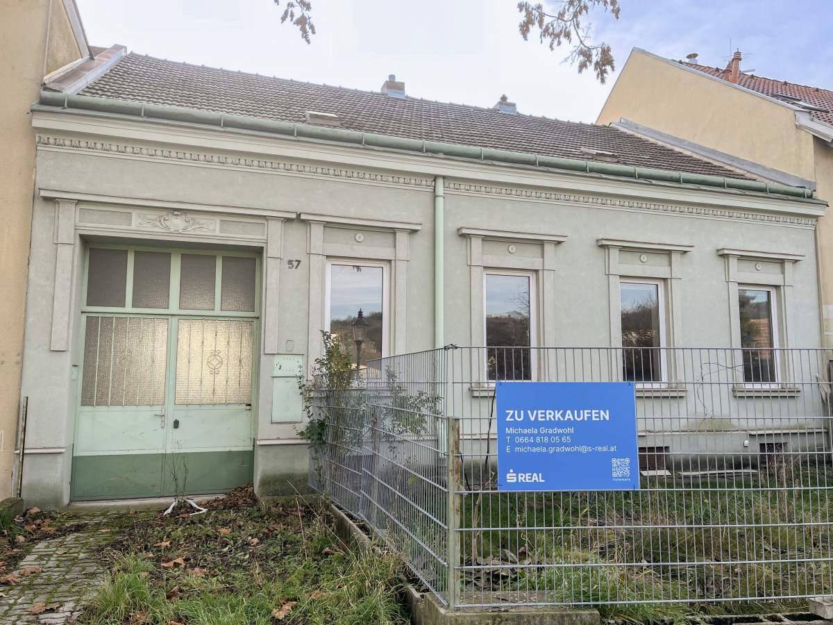 Vorderansicht eines älteren Gebäudes mit Verkaufsanzeige und Renovierungsbedarf.