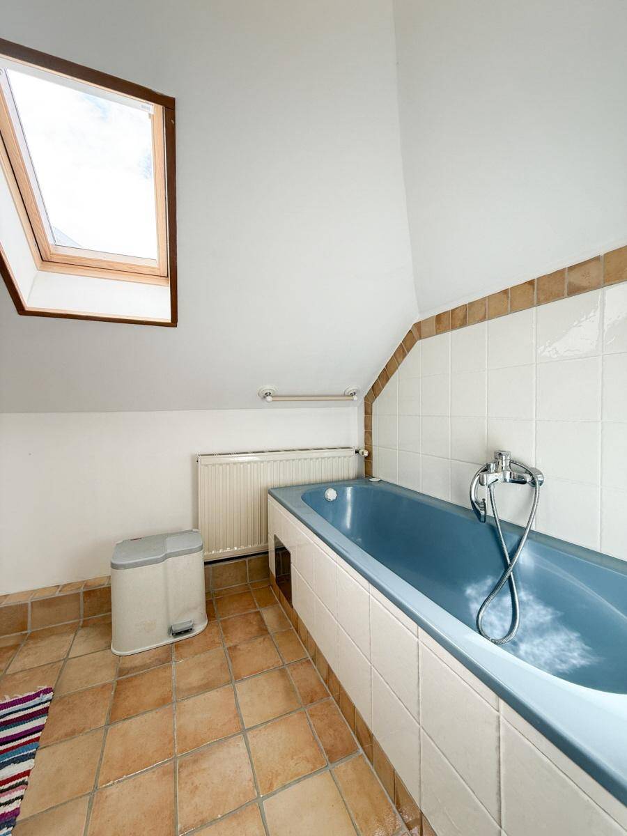 Dachgeschoss-Badezimmer mit blauer Badewanne, Terrakottafliesen und Dachfenster.