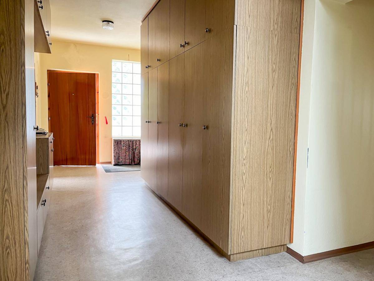 Eingangsbereich mit langen Einbauschränken und einer Holztür, die zum Außenbereich führt.