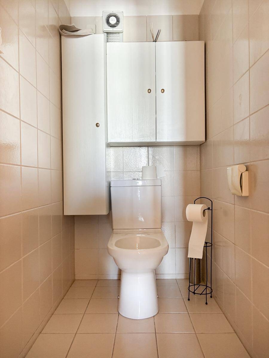 Separate Toilette mit beigefarbenen Fliesen und Wandschränken.