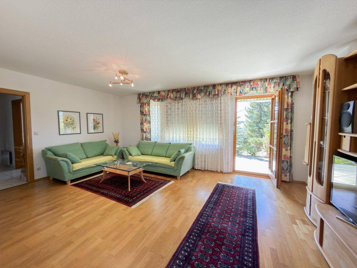 Gemütliches Wohnzimmer mit Holzboden, grünen Sofas und Zugang zum Garten.