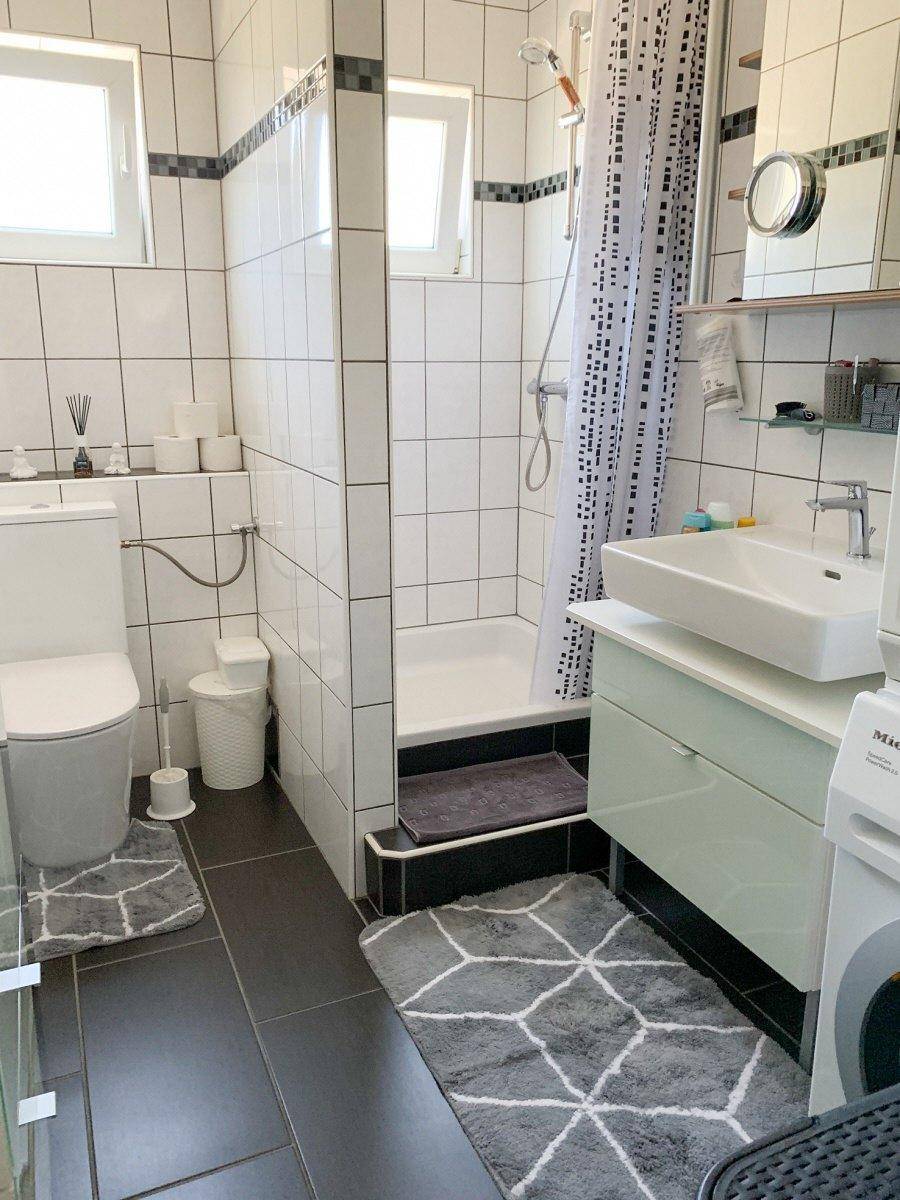 Modernes Badezimmer mit weißen Fliesen, ebenerdiger Dusche und Fenster für Tageslicht.