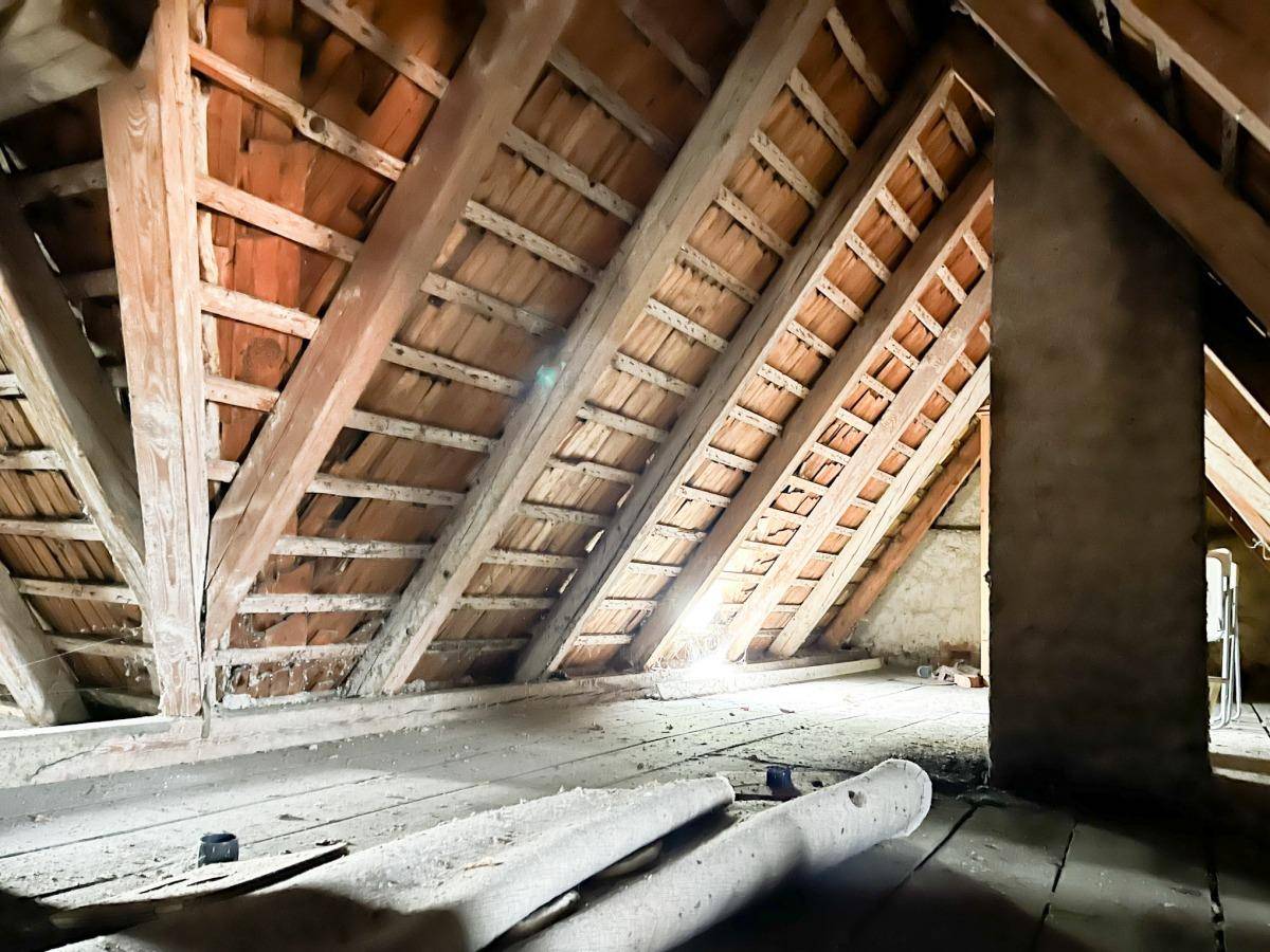 Unausgebauter Dachboden mit sichtbaren Holzbalken und Ziegeln.