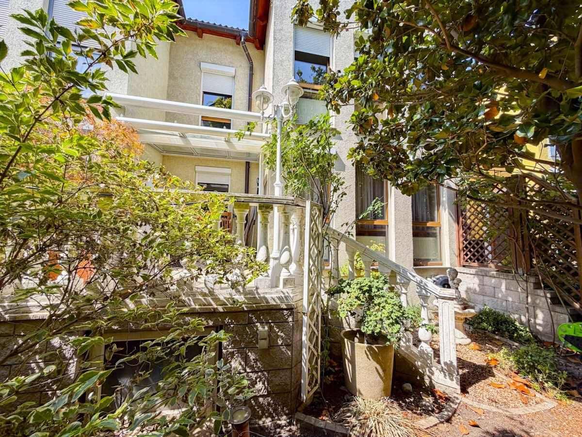 Gartenansicht mit Steintreppe, Balustrade und einem überdachten Bereich am Haus.