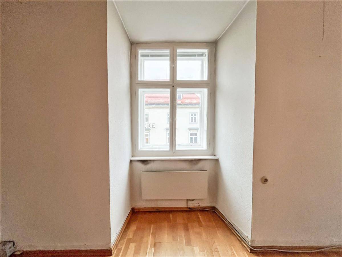 Kleiner, leerer Raum mit Holzboden und einem einzelnen Fenster, das den Blick nach draußen freigibt.