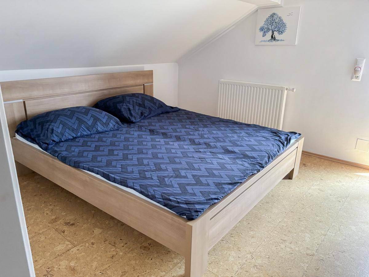 Schlafzimmer im Dachgeschoss mit Holzbett und Korkboden unter einer Dachschräge.