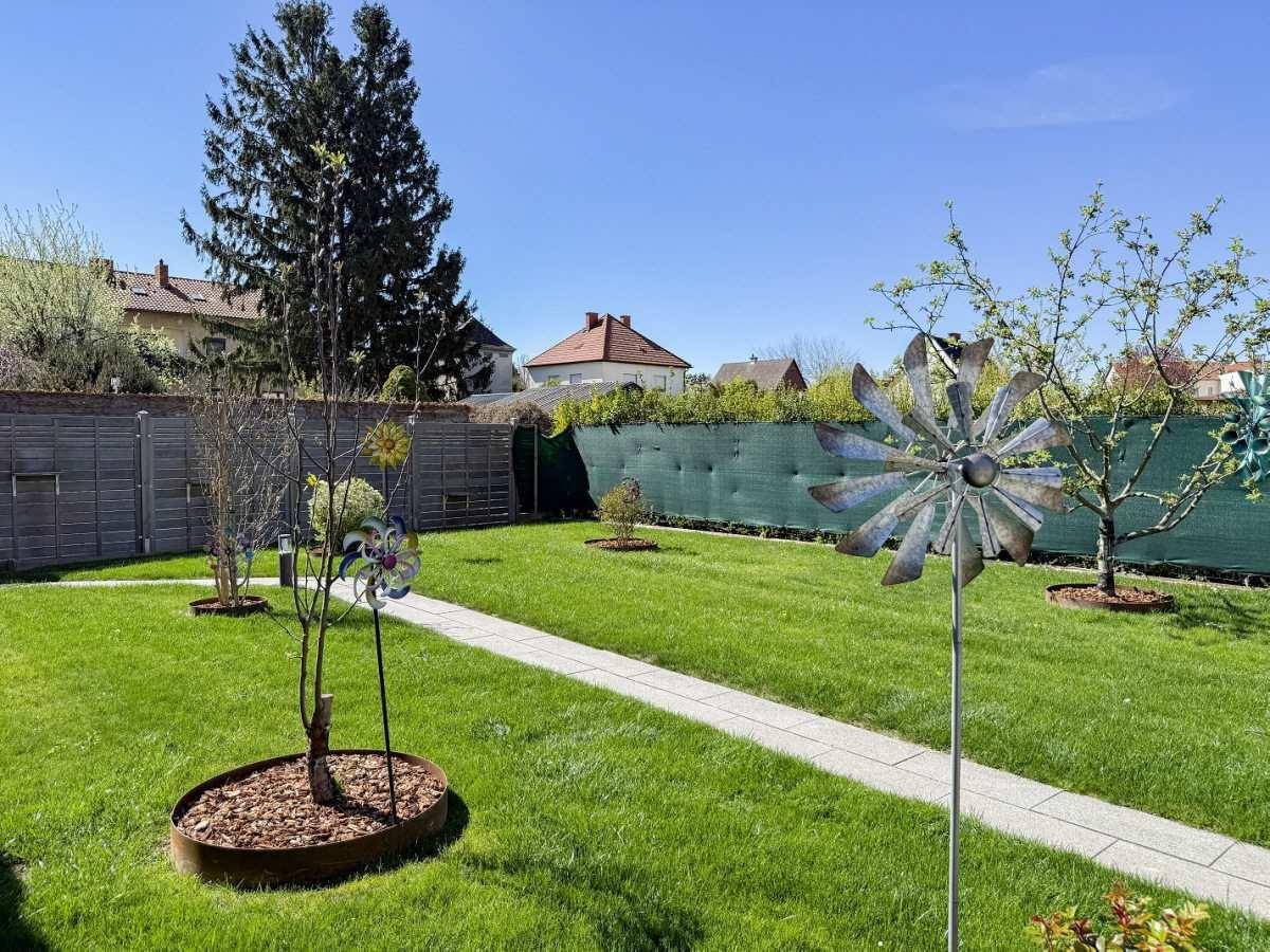 Sonniger Garten mit Rasen, dekorativen Windspielen und einem gepflasterten Weg.