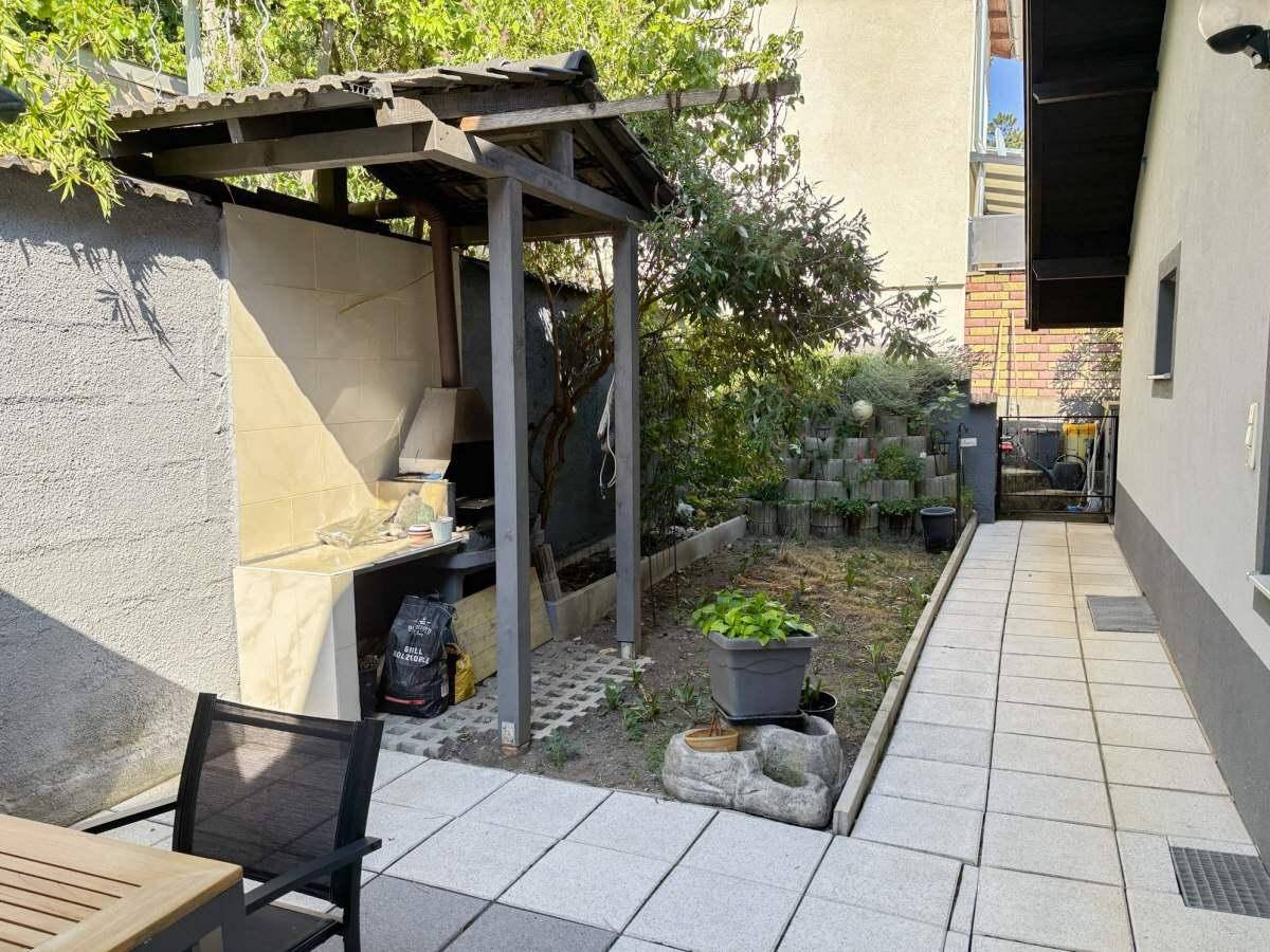 Gartenbereich mit gepflasterter Fläche, Grillplatz und Grünflächen.