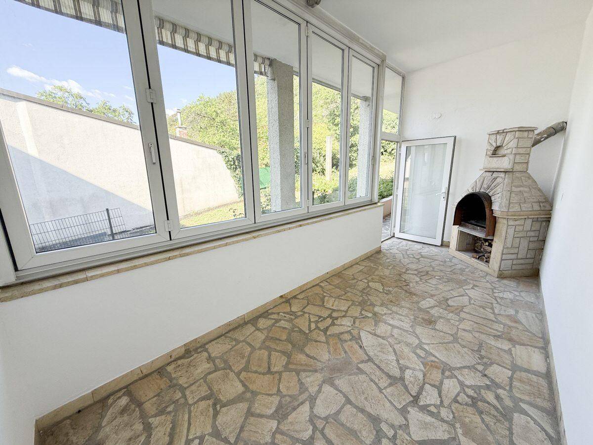 Verglaster Wintergarten mit Steinboden und integriertem Grillkamin für gesellige Abende.