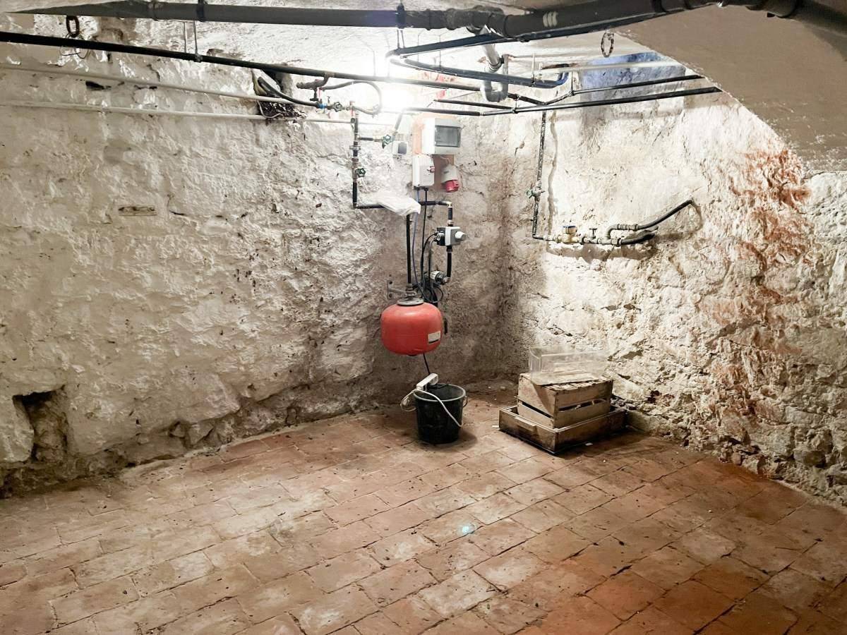 Rustikaler Kellerraum mit Ziegelboden, weiß getünchten Wänden und sichtbaren Rohren.