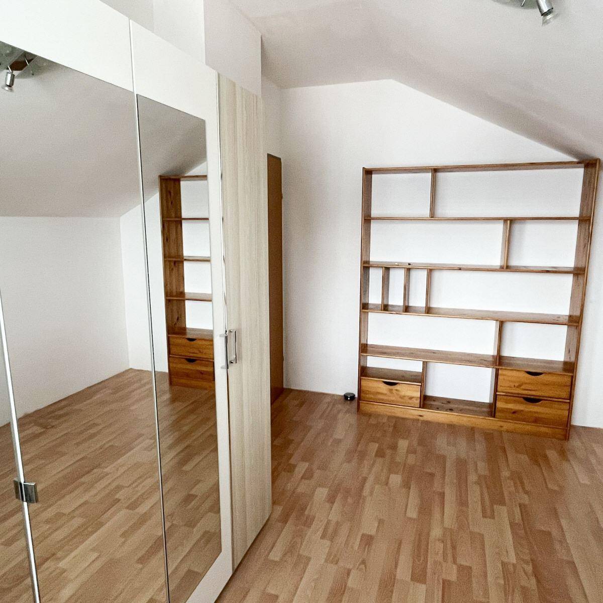 Dachzimmer mit Holzboden, Dachschräge und großem Spiegelschrank, hell und geräumig.